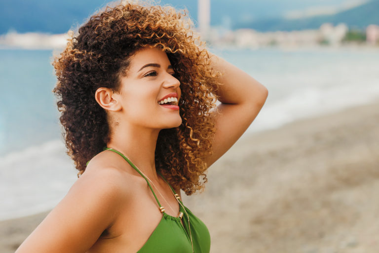 Fine and coily 3c hair smiling woman at beach