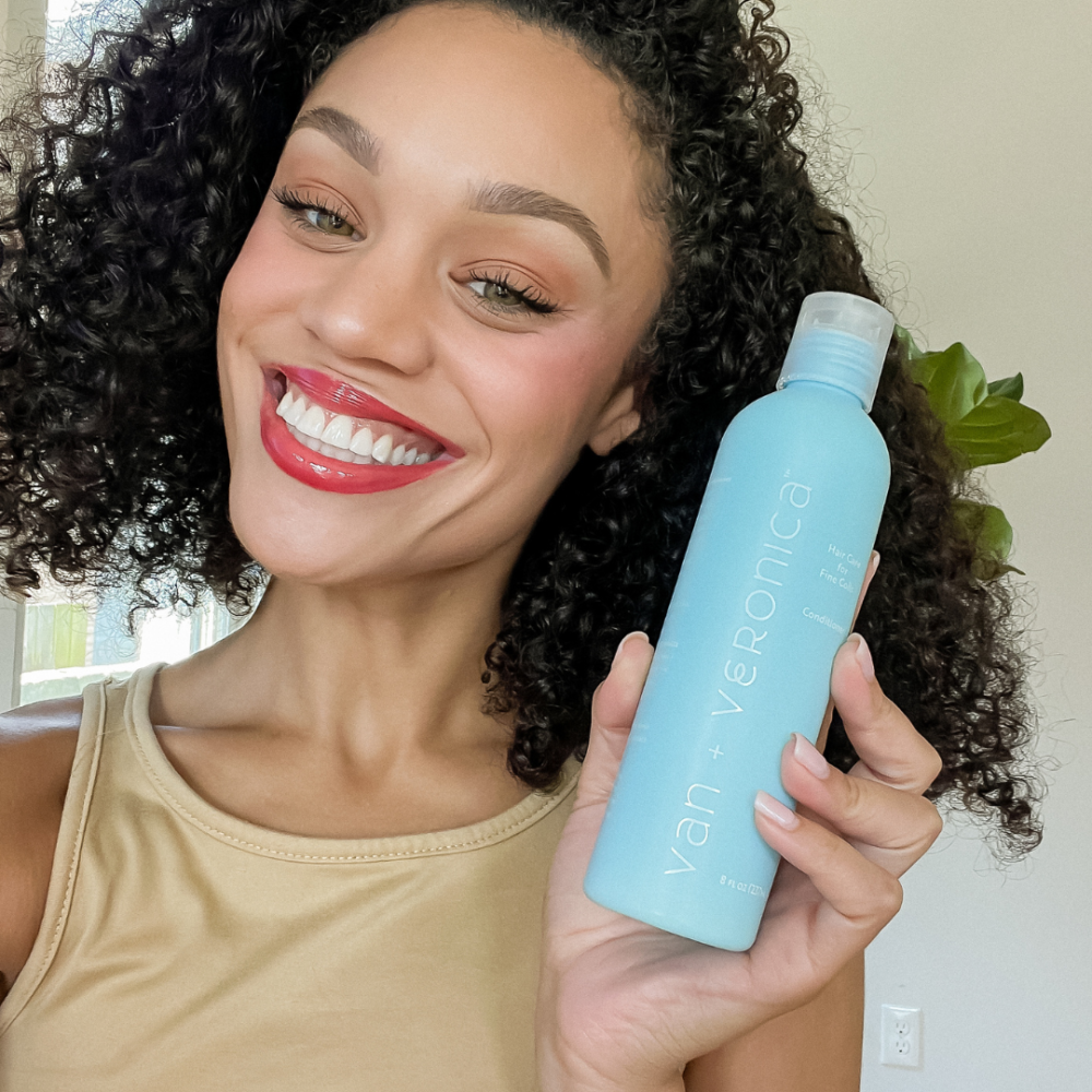 Image of beautiful woman holding van + veronica Haircare Conditioner for fine curly hair