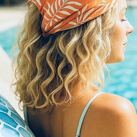 woman with blonde fine curly hair, relaxing by swimming pool